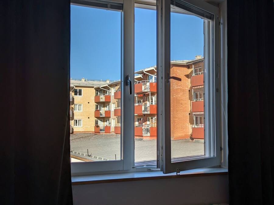 A window with a view of multi-story buildings, including a brick structure with balconies.