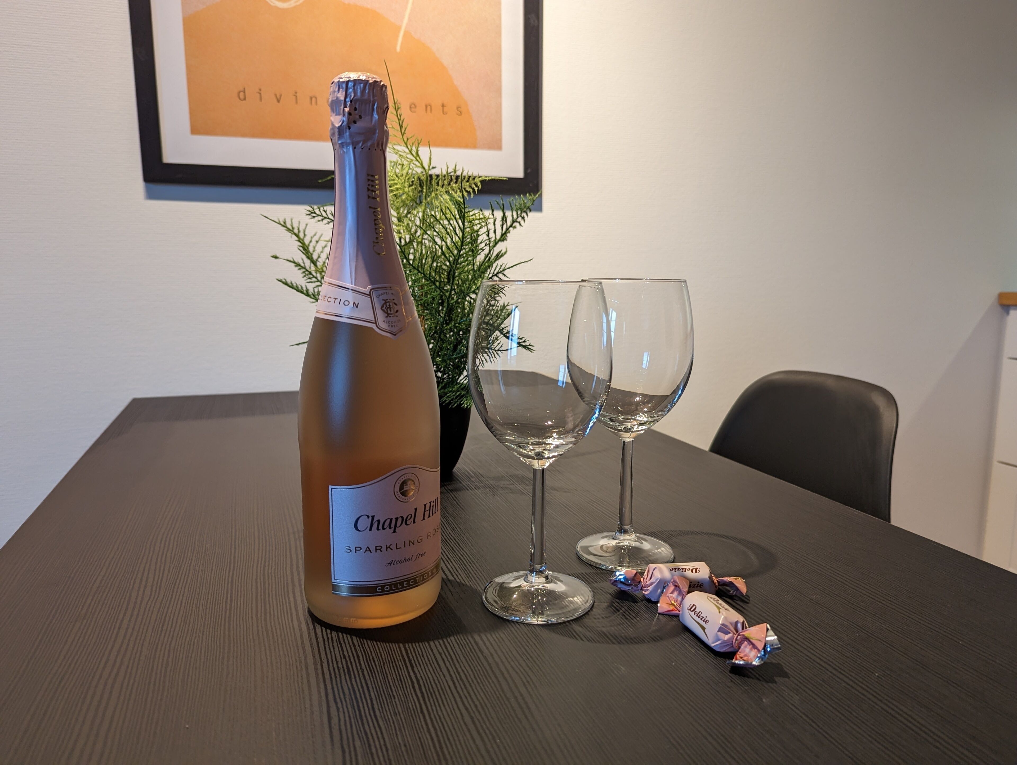 A bottle of Chapel Hill Sparkling Rosé, two empty wine glasses, and some wrapped candies on a table.
