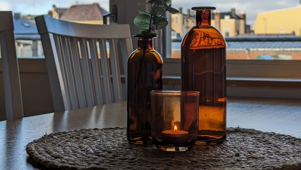 A table with a candle, a glass, and two bottles on a woven placemat. - Hotell Bro (Kristinehamn)