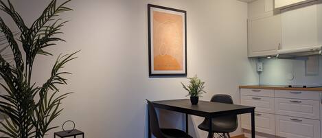 A modern kitchen with white cabinets, a dining table with two chairs, a potted plant, and a framed artwork on the wall.