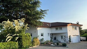 A two-story house with a tiled roof, a front porch, and a paved driveway. - Vacation apartment Freiburg surroundings - FELDSCHLÖSSCHEN in March (March)