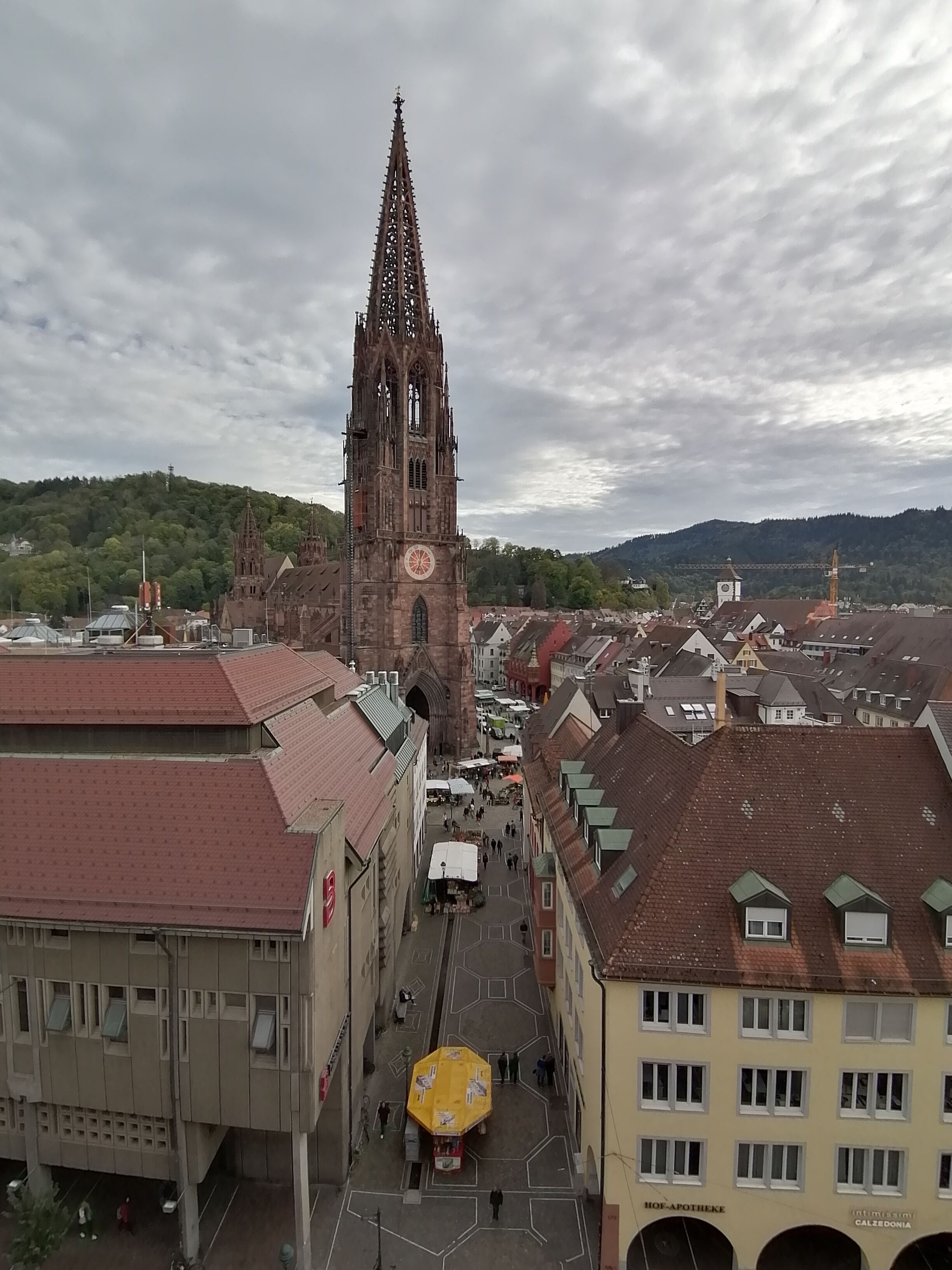 A historic church with a tall spire, a central square with market stalls, and surrounding buildings with varied rooflines.