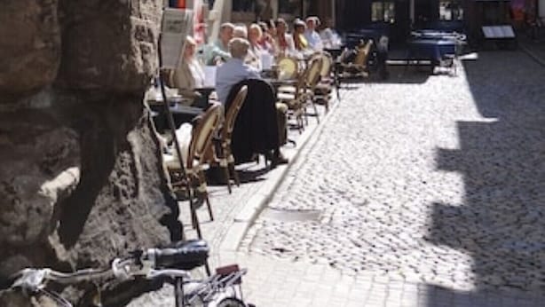 Una calle empedrada con mesas de café al aire libre, un edificio de piedra y un edificio con un letrero que dice "Kulturhaus".