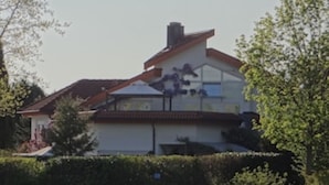 Una casa de dos pisos con techo inclinado, una chimenea visible y un ventanal grande en el segundo piso.