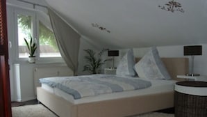 Un dormitorio con cama, mesitas de noche, lámpara, planta en maceta y ventana.