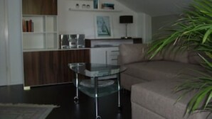 Una sala moderna con un sofá, una mesa de centro de vidrio, una estantería y una planta.
