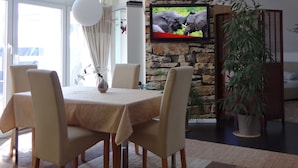 Un área de comedor con una mesa dispuesta para cuatro, una pared de acento de piedra, un televisor montado en la pared y una planta en maceta.