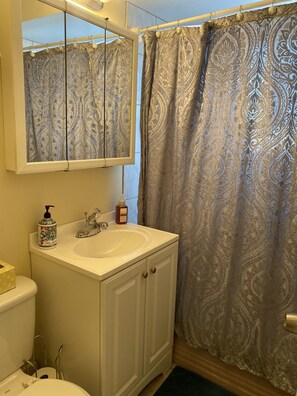 Une salle de bain avec un lavabo blanc, un miroir au-dessus et un rideau de douche à motifs.