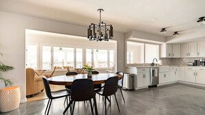 A modern kitchen with white cabinets, a central island, and a dining area with a round table and chairs.