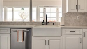 A kitchen with white cabinets, a stainless steel refrigerator, a double sink, and a window with a view of the outside.