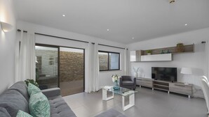 Ein modernes Wohnzimmer mit einem grauen Sofa, einem Glastisch, einem Fernseher und einem Kamin.