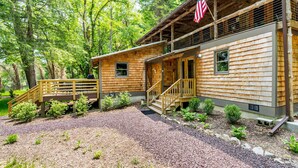 A rustic cabin with a wooden exterior, a porch with a wooden railing, and an American flag. - Log cabin w/riverfront & hot tub (Rileyville)