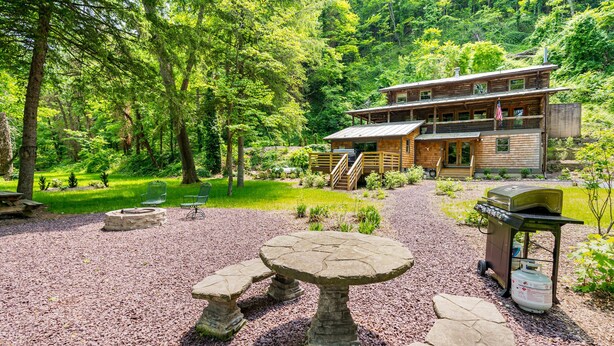 A rustic lodge with a stone patio, outdoor seating, and a grill area. - Log cabin w/riverfront & hot tub (Rileyville)