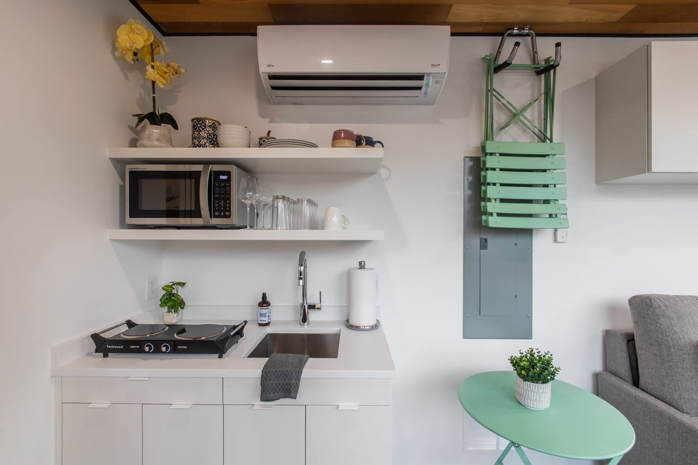 A compact kitchen with a microwave, stove, sink, and a small table with a plant.