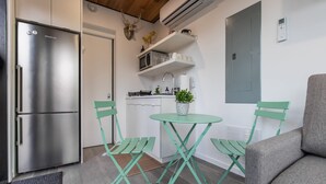 A compact kitchen with a stainless steel refrigerator, a small dining table with green chairs, and a grey sofa. - Riverside Tiny Cabin w Hot Tub, Fire Pit, & Kayaks (Luray)
