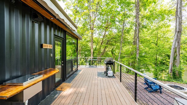 A wooden deck with a bench and a grill, overlooking a forested area. - Riverside Tiny Cabin w Hot Tub, Fire Pit, & Kayaks (Luray)