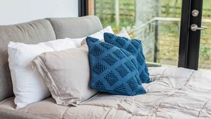 A bed with a beige duvet, white pillows, and a blue knitted throw. - Riverside Tiny Cabin w Hot Tub, Fire Pit, & Kayaks (Luray)