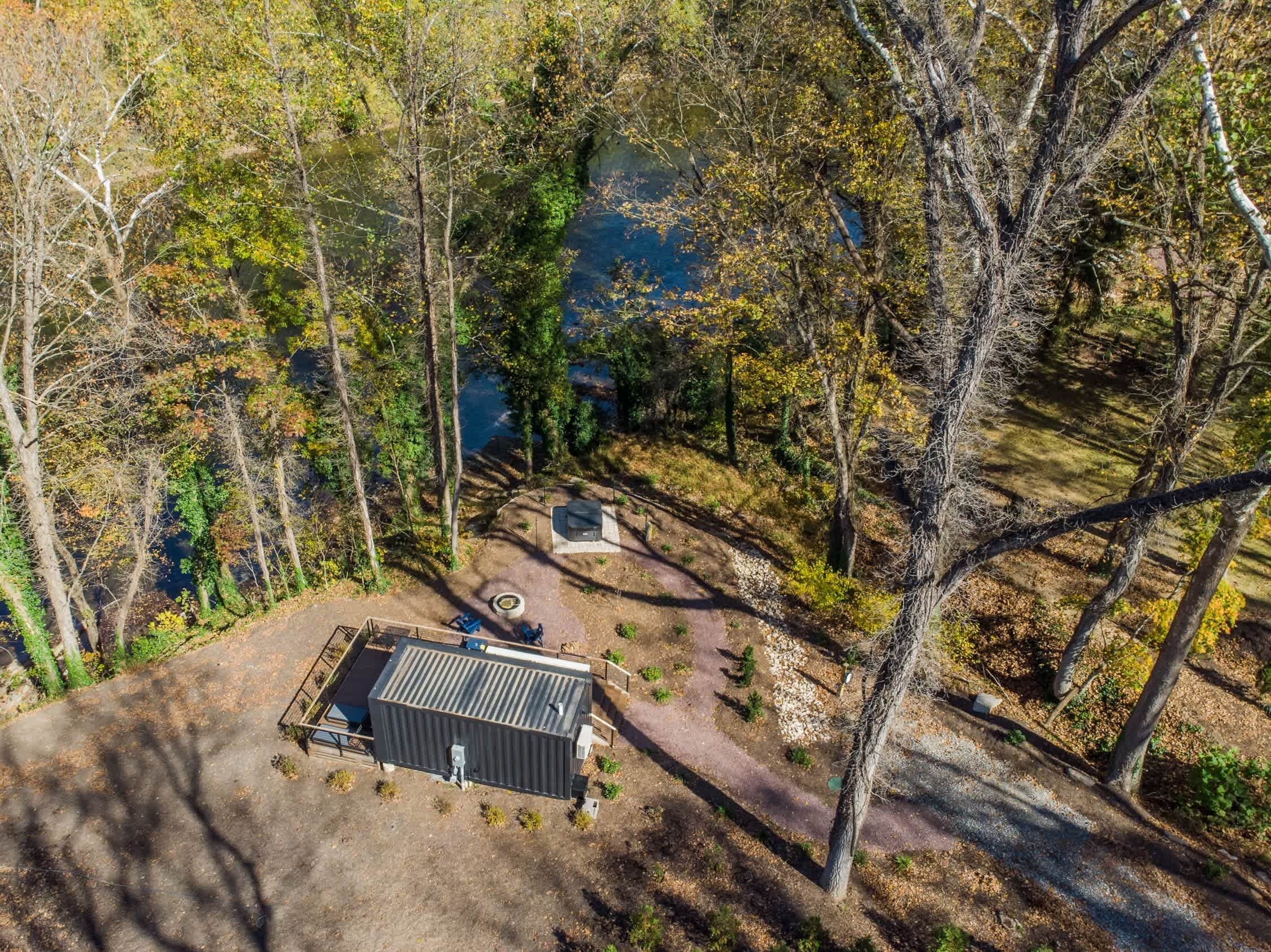 An aerial view of a cabin with a metal roof, surrounded by trees and a small pond.