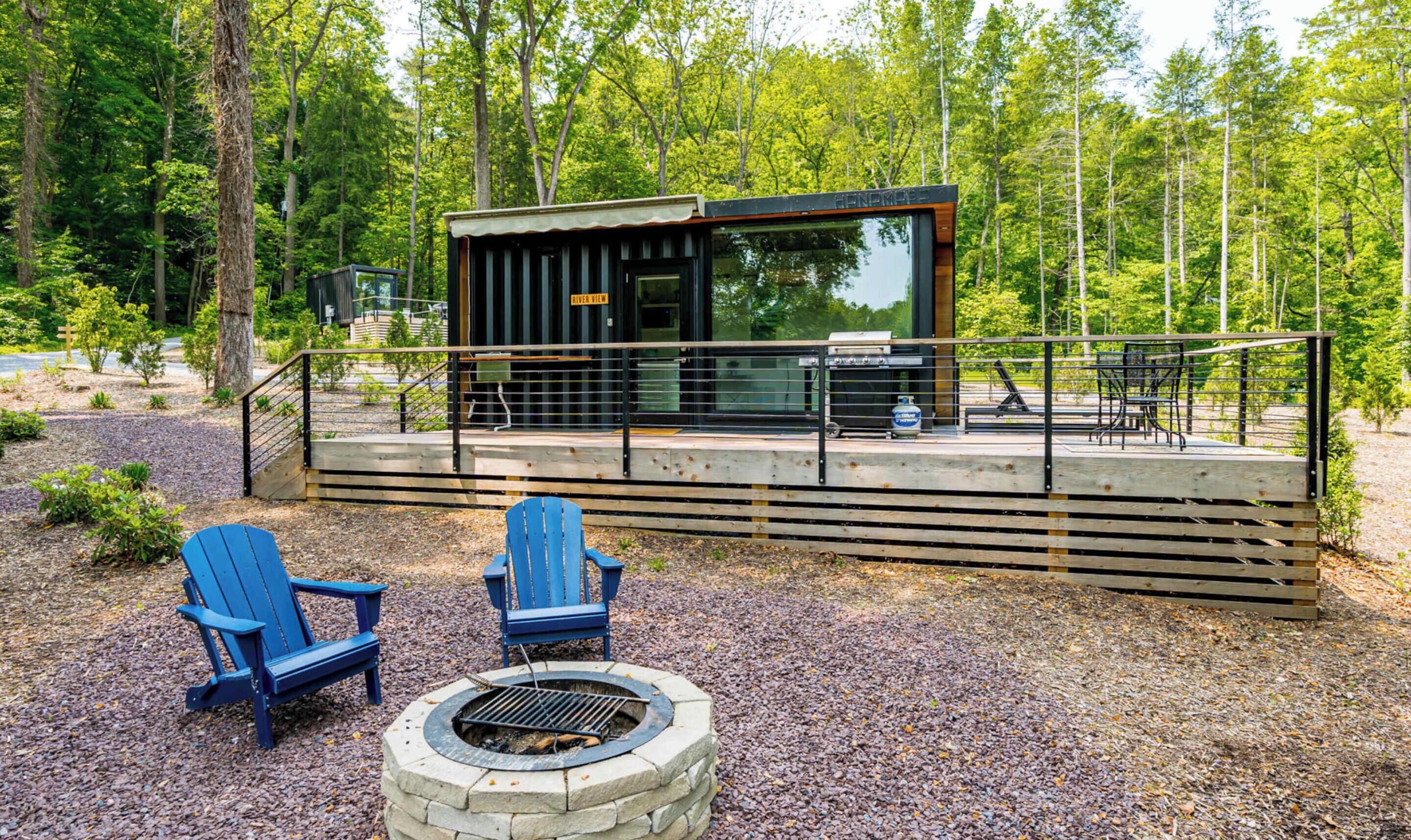 A cabin with a deck, two Adirondack chairs, and a fire pit.