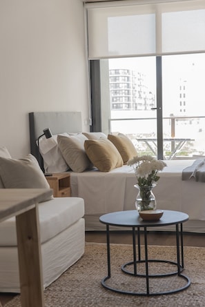 A modern bedroom with a bed, bedside table, and a round table with a vase of flowers.