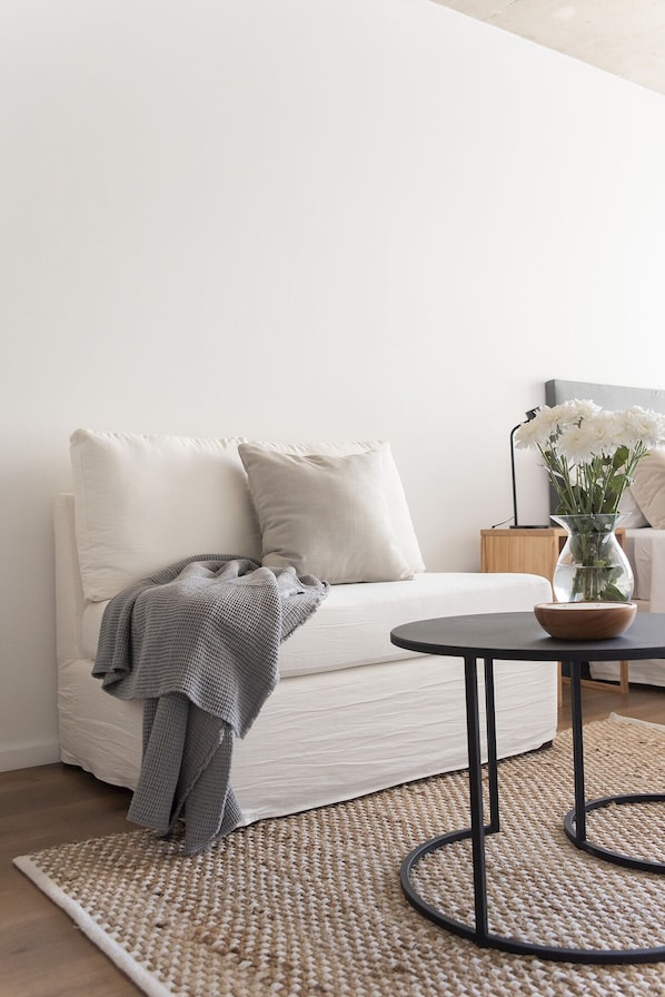 A minimalist living room with a white sofa, a round coffee table, and a woven rug.