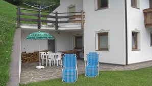 Un bâtiment à deux étages doté d’un balcon, d’un espace extérieur aménagé avec une table et des chaises, et d’une terrasse couverte également équipée d’une table et de chaises.
