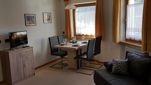 Un espace de vie compact comprenant une table à manger, des chaises, un téléviseur posé sur un meuble, un canapé et une fenêtre avec des rideaux.