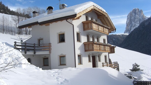 Un chalet à deux étages, doté de balcons en bois, se dressant sur un fond de montagnes enneigées.