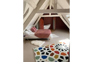 A cozy, triangular room with a bed, a white chair, and a colorful rug. - La Maîtrise, in the heart of Bayeux Les Maisons des Pommiers (Bayeux)