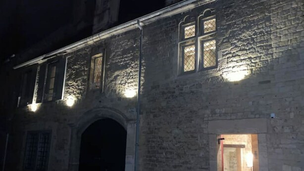 Um edifício de pedra com uma entrada em arco e uma pequena janela iluminada.