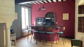 Uma sala de jantar com uma mesa redonda e seis cadeiras, uma cozinha com fogão e armários, e uma janela ampla que oferece iluminação natural.