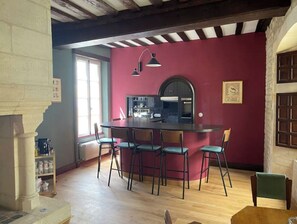 A dining area with a round table and six chairs, a kitchen area with a stove and cabinets, and a large window providing natural light. - La Maîtrise, in the heart of Bayeux Les Maisons des Pommiers (Bayeux)