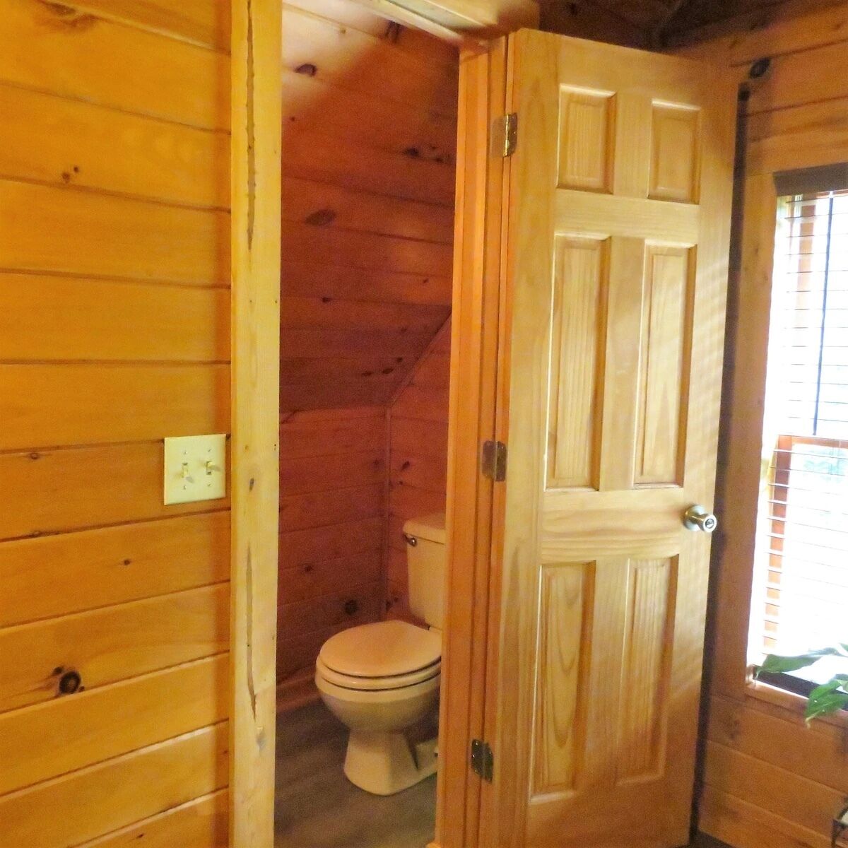 Baño de cabaña de madera con inodoro y una puerta que da a otra habitación.
