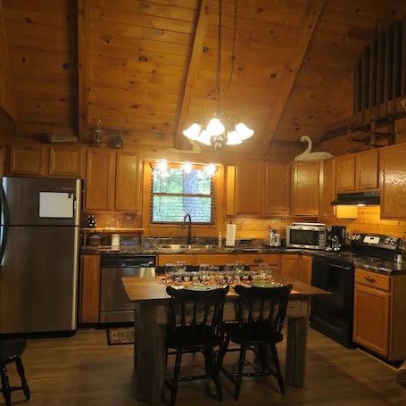 A cozy kitchen with wooden cabinets, a stainless steel refrigerator, a microwave, a stove, and a dining area with chairs and a table.