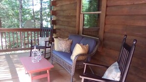 Eine Holzterrasse mit einer Rattan-Couch, einem roten Tisch und einem schwarzen Stuhl.