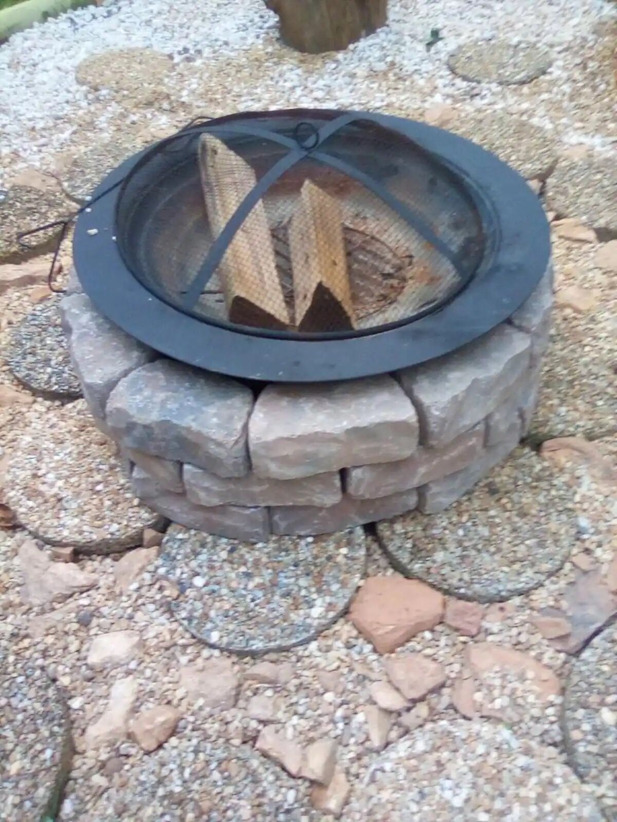 Una chimenea de piedra con una protección metálica y leña en su interior.