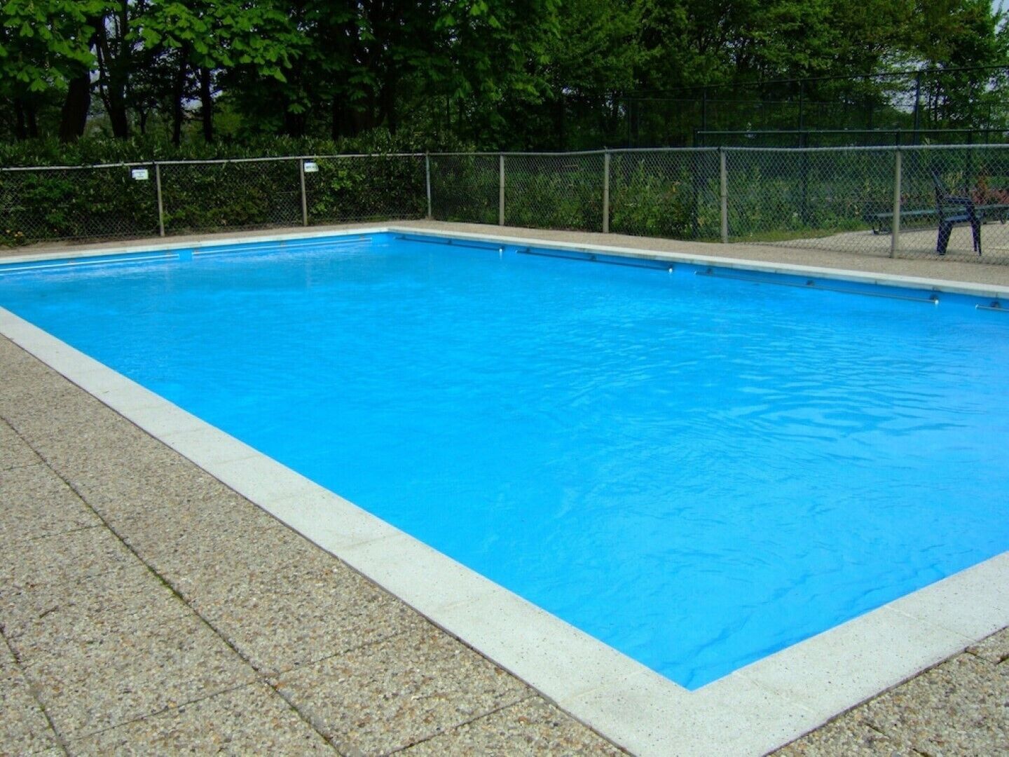 A rectangular swimming pool with a tiled edge and a fence surrounding it.