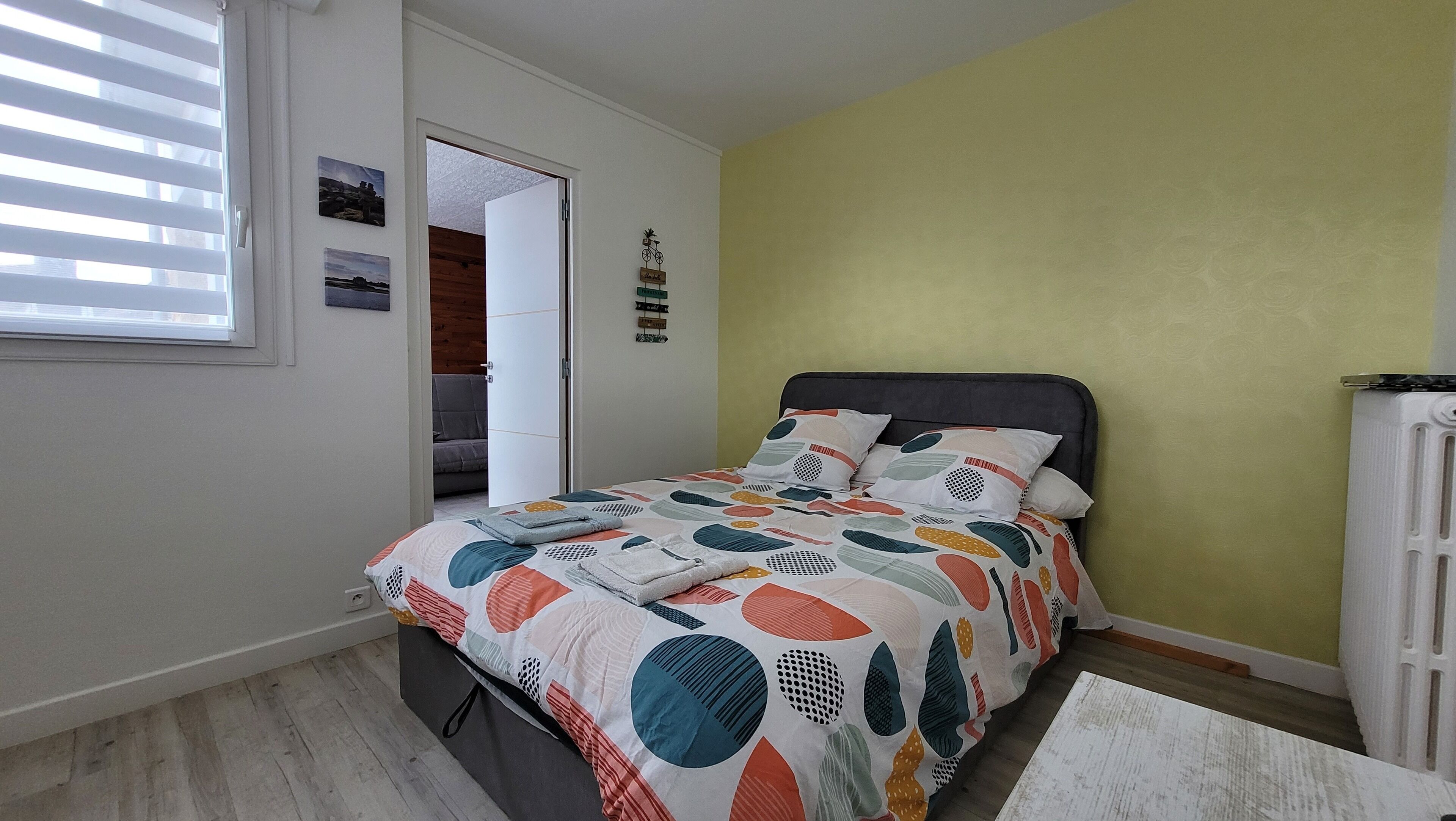 A bedroom with a bed, a window with blinds, a door leading to another room, and a radiator.