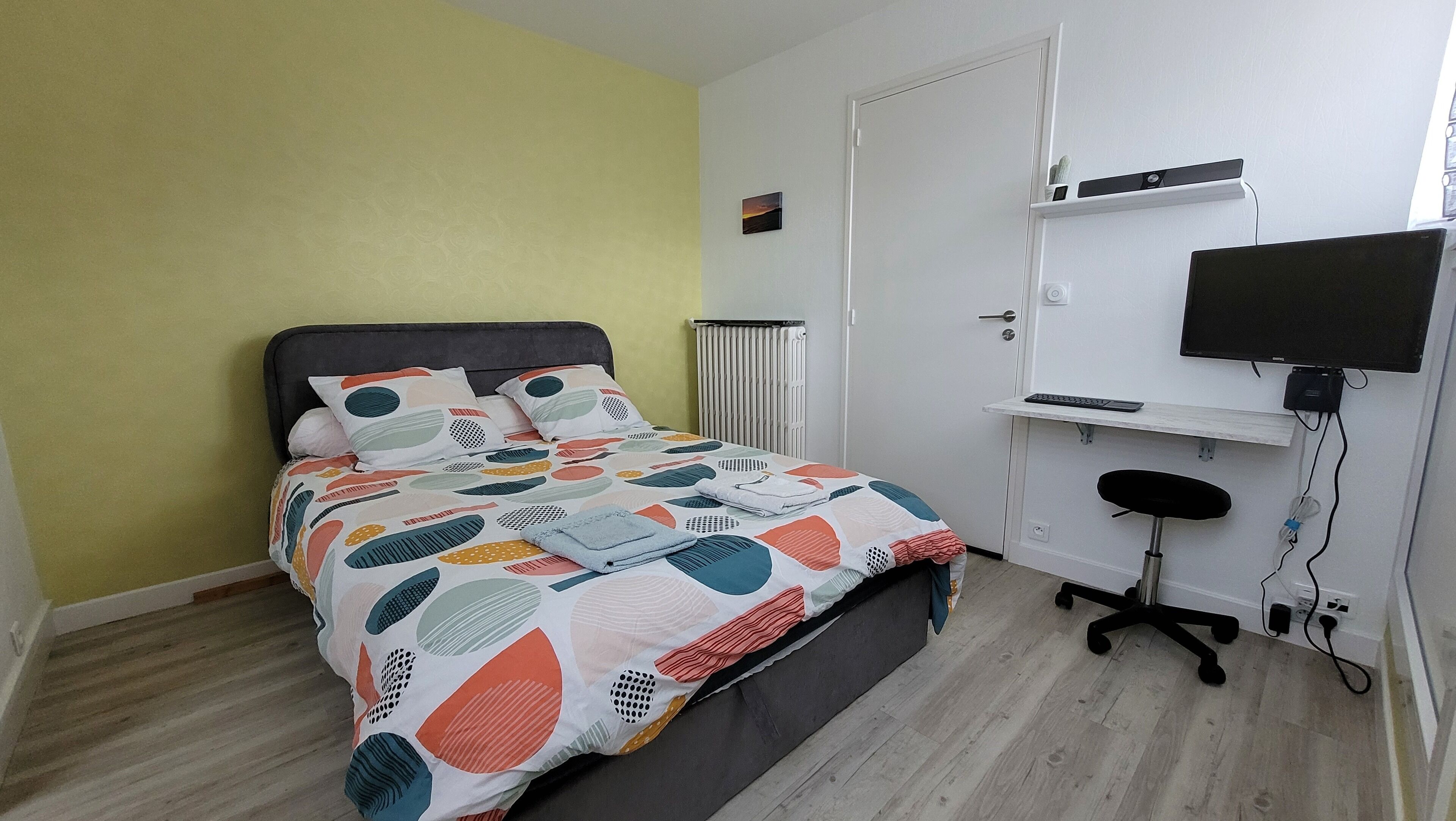 A bedroom with a bed, a desk, a chair, a radiator, and a TV.