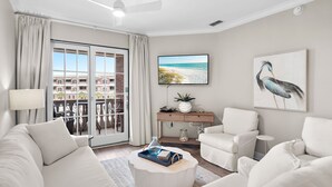 Una sala de estar con sofá, sillones, una mesa de centro, televisor, un cuadro y un balcón con vistas.