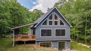 Ein zweistöckiges Haus mit einer großen Terrasse, umgeben von einem Wald.