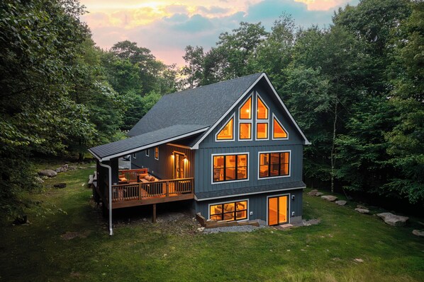 A two-story cabin with a deck and large windows, surrounded by trees.