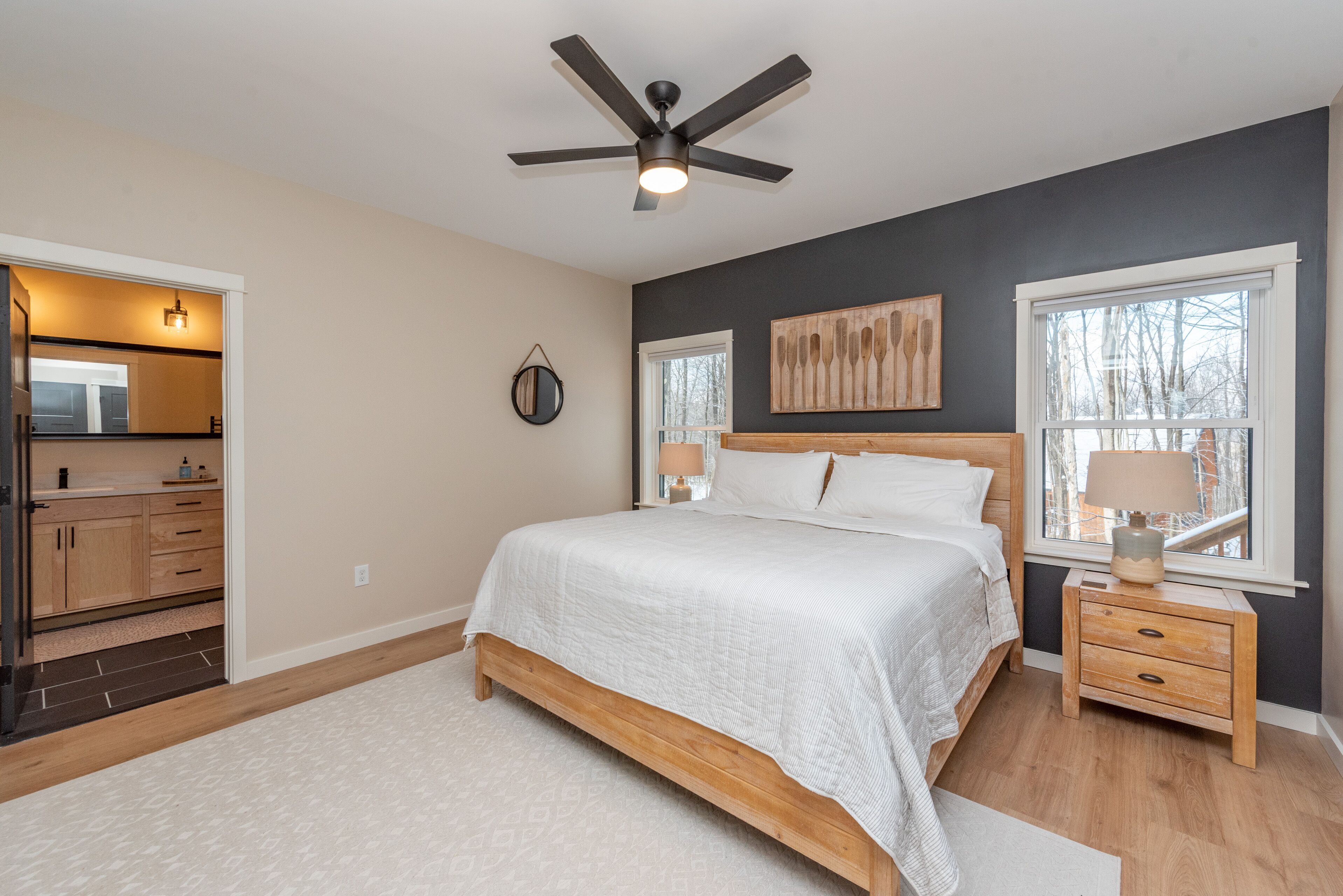 A bedroom with a bed, bedside tables, a ceiling fan, and a window with a view.