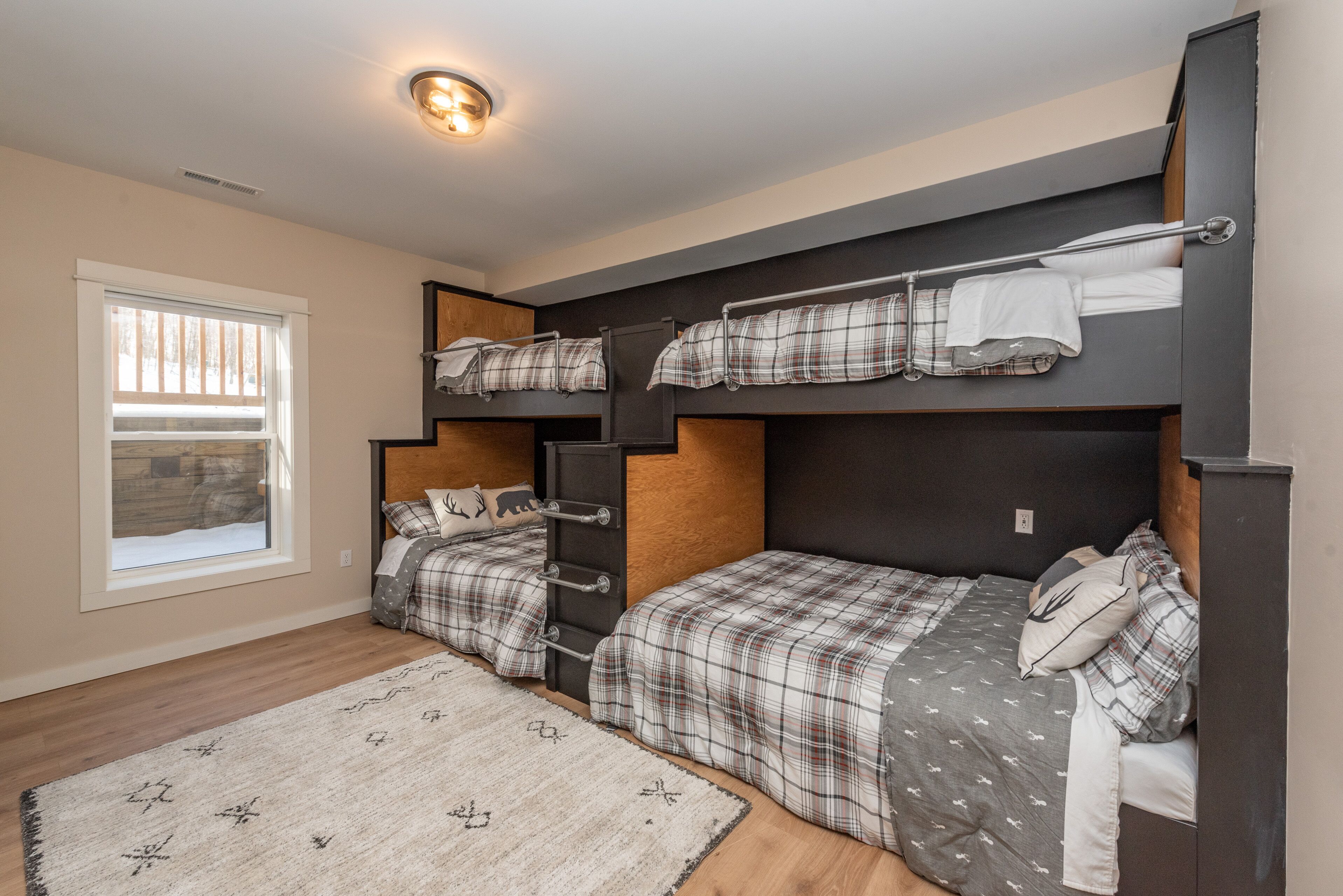 A bedroom with bunk beds, a window with blinds, a wooden floor, and a rug.
