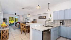 A modern kitchen with blue cabinets, a marble countertop, and pendant lighting.
