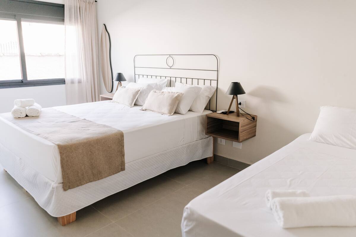 A neatly arranged bedroom with a large bed, bedside tables, and a window with curtains.
