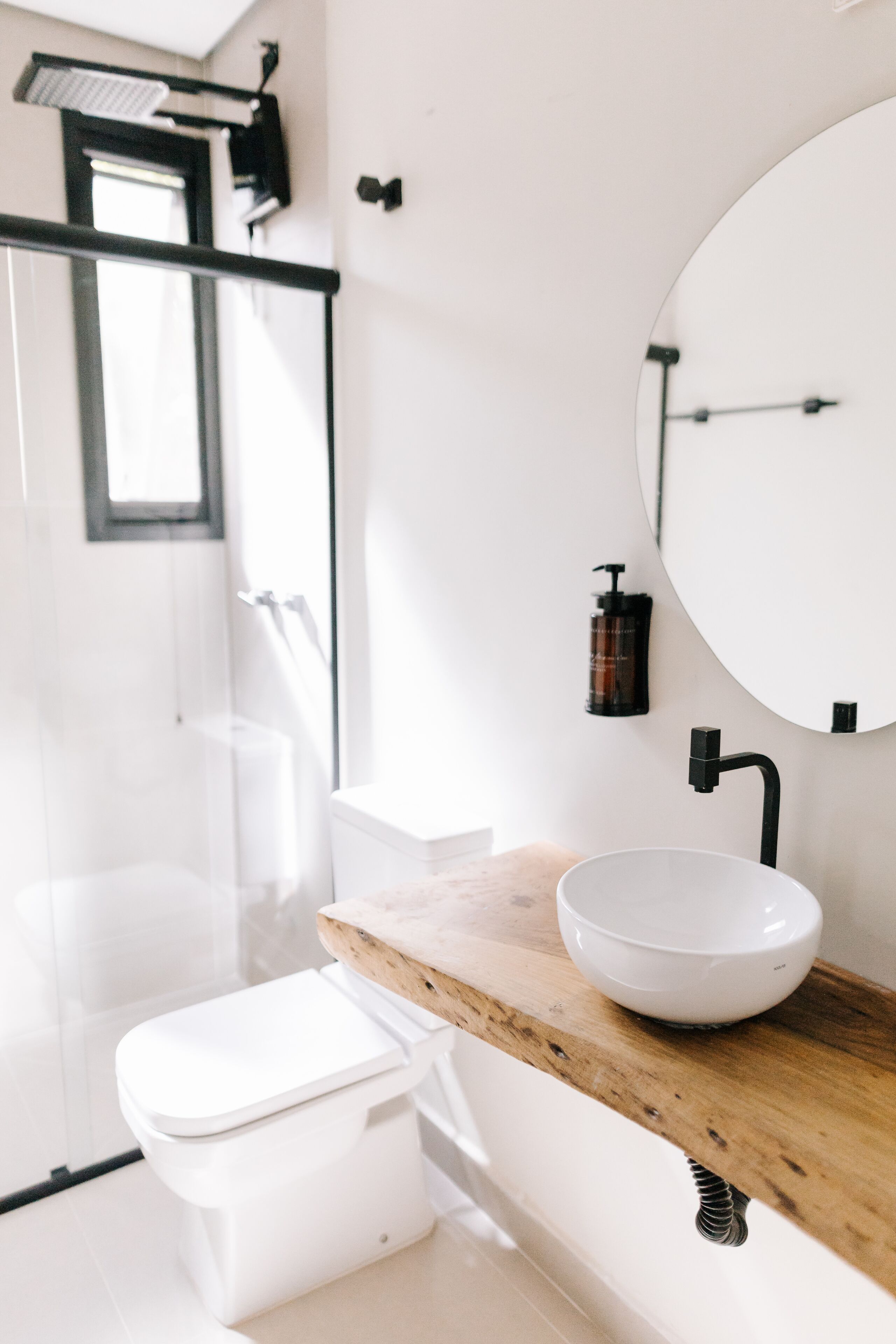 Un baño moderno con cabina de ducha de vidrio, inodoro blanco, tocador de madera con lavamanos blanco y un espejo grande.