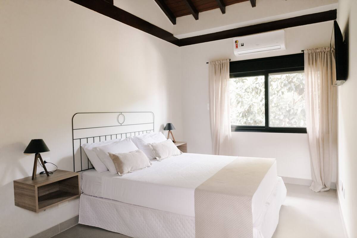 A neatly arranged bedroom with a bed, bedside tables, and a window with curtains.