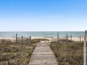 A wooden boardwalk leading to a beach with a fence on either side.