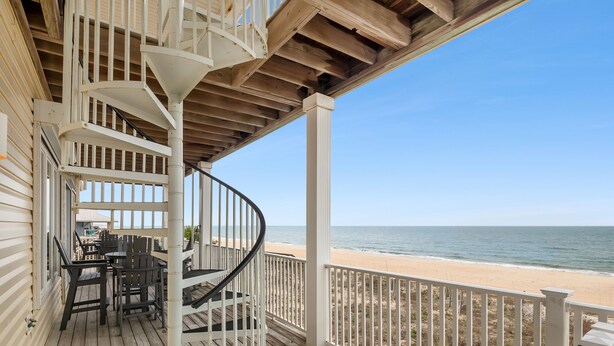 A wooden deck with a spiral staircase, outdoor seating, and a view of the beach. - Beach Buzz: Beachfront, Private Pool, Hot Tub (St. George Island)